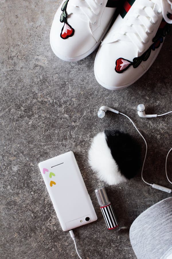 Dziewczyny ` s akcesoria - biały smartphone, słuchawki, sneakers i siwieją nakrętkę obraz stock Dziewczyny ` s akcesoria - biały smartphone, słuchawki, sneakers i siwieją nakrętkę obraz stock