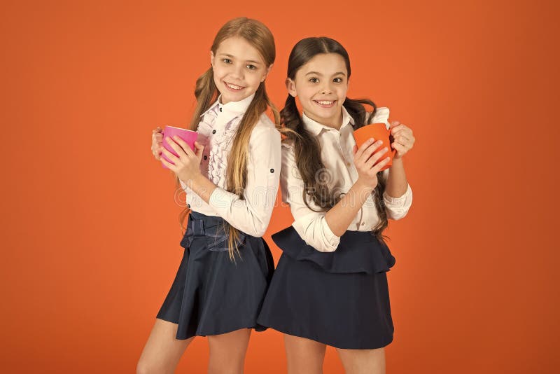 Girls kids school uniform orange background. Schoolgirl hold mug. School lunch. Having break relax. Drinking tea while break. School mates relaxing with drink. Hydration and water regime. Tea break. Girls kids school uniform orange background. Schoolgirl hold mug. School lunch. Having break relax. Drinking tea while break. School mates relaxing with drink. Hydration and water regime. Tea break.