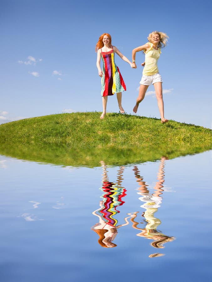 Two happy girls fleeing on a meadow. Reflected in water. Against the backdrop of blue sky. Two happy girls fleeing on a meadow. Reflected in water. Against the backdrop of blue sky.