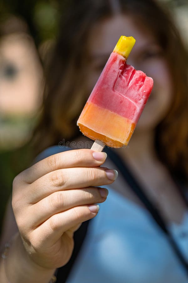 Dziewczęta trzymające gorzko żółte czerwone lody z owocami na drewnianym patyku. truskawkowy smak mango wiśniowego. słoneczny zdjęcia stock
