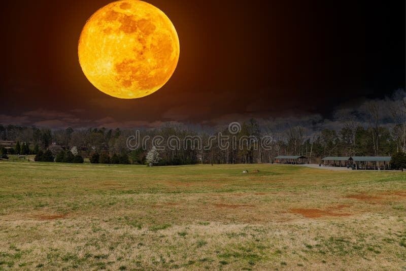 A spring day in the park with green and yellow grass, a smooth winding footpath, buildings and pergolas with bare winter trees and powerful red moon at night at Swift Cantrell Park in Kennesaw Georgia USA. A spring day in the park with green and yellow grass, a smooth winding footpath, buildings and pergolas with bare winter trees and powerful red moon at night at Swift Cantrell Park in Kennesaw Georgia USA