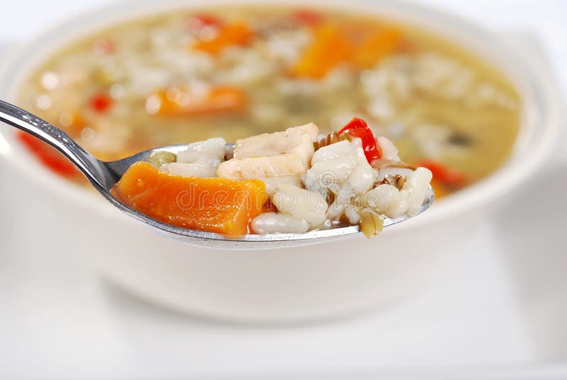 Closeup of a spoonful chicken and wild rice soup with bowl in the background. Closeup of a spoonful chicken and wild rice soup with bowl in the background