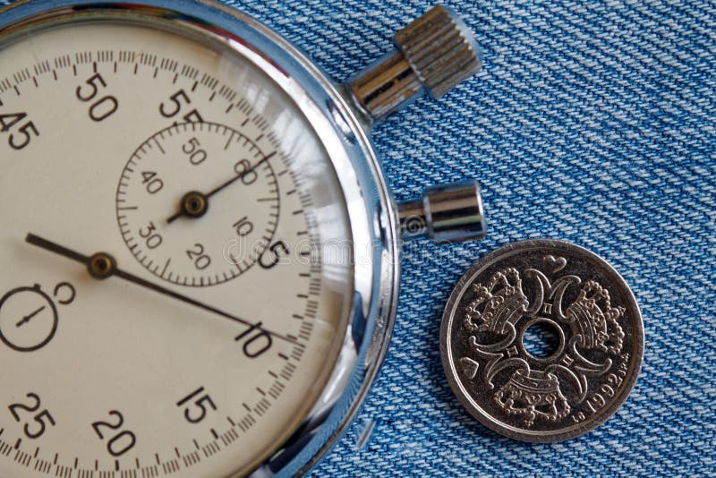 Dänemark-Münze mit einer Bezeichnung von einer Krone (Krone) (Rückseite) und von Stoppuhr auf abgenutztem Blue Jeans-Hintergrund lizenzfreie stockbilder Dänemark-Münze mit einer Bezeichnung von einer Krone (Krone) (Rückseite) und von Stoppuhr auf abgenutztem Blue Jeans-Hintergrund lizenzfreie stockbilder