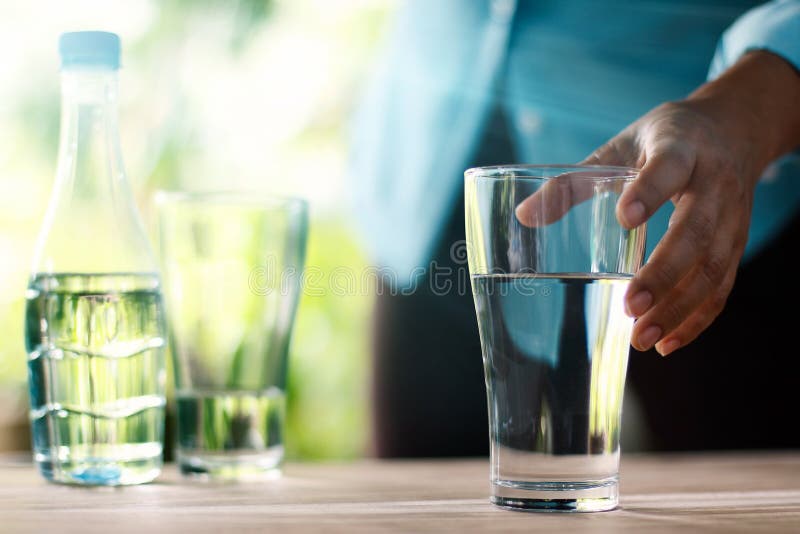 Dé alcanzar para el vidrio de agua potable en la tabla de madera imagenes de archivo Dé alcanzar para el vidrio de agua potable en la tabla de madera imagenes de archivo