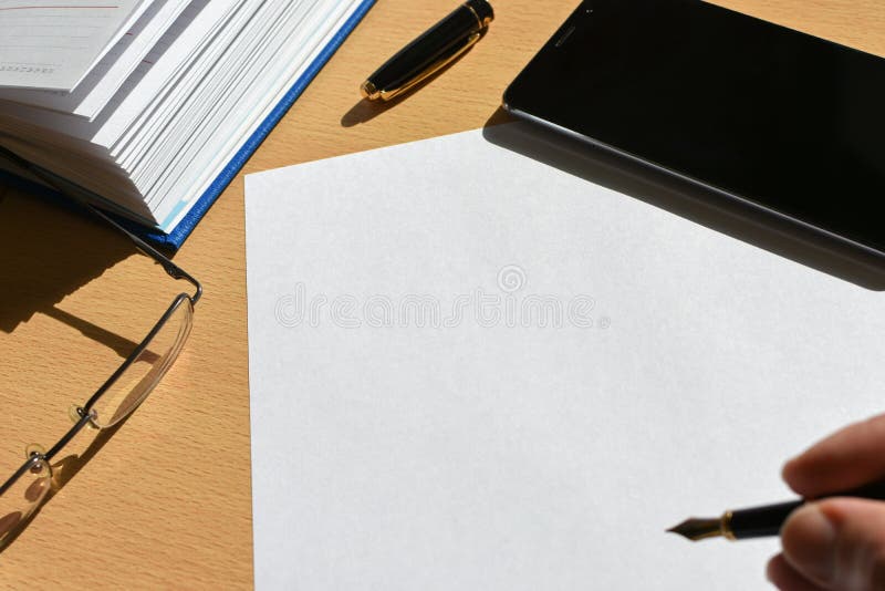 Dé la pluma en una hoja de papel en una mesa de madera en la oficina, smartphone, efectos de escritorio, vidrios, espacio de la e fotografía de archivo Dé la pluma en una hoja de papel en una mesa de madera en la oficina, smartphone, efectos de escritorio, vidrios, espacio de la e fotografía de archivo