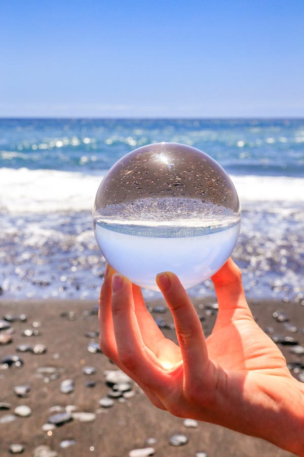Dé sostener la esfera de cristal en la playa y el mar fotos de archivo libres de regalías Dé sostener la esfera de cristal en la playa y el mar fotos de archivo libres de regalías