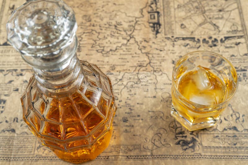 Décanteur de whiskey ou d'eau-de-vie fine avec un verre de whiskey sur une table, couvert dans la vieille carte de papier parchem images stock Décanteur de whiskey ou d'eau-de-vie fine avec un verre de whiskey sur une table, couvert dans la vieille carte de papier parchem images stock
