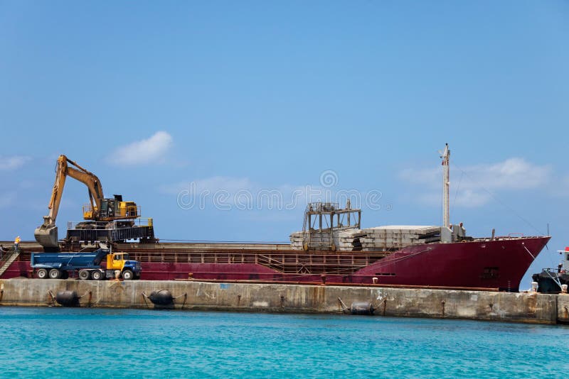 Excavator on top of a docked ship offloads dirt into a dump truck. Excavator on top of a docked ship offloads dirt into a dump truck