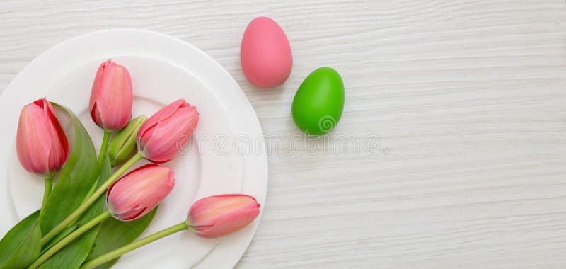 Décoration de table de pâques. couleur pastel d'oeuf dans l'assiette et tulipe rose sur le bois blanc au-dessus