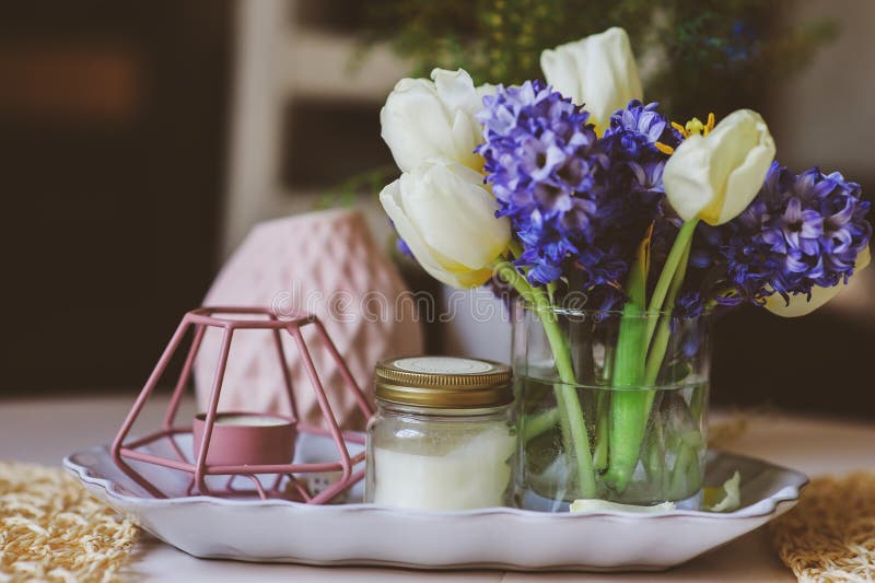 Spring decorations at home on the table in modern scandinavian style with flowers and aromatic candles. Slow living and hygge concept. Spring decorations at home on the table in modern scandinavian style with flowers and aromatic candles. Slow living and hygge concept