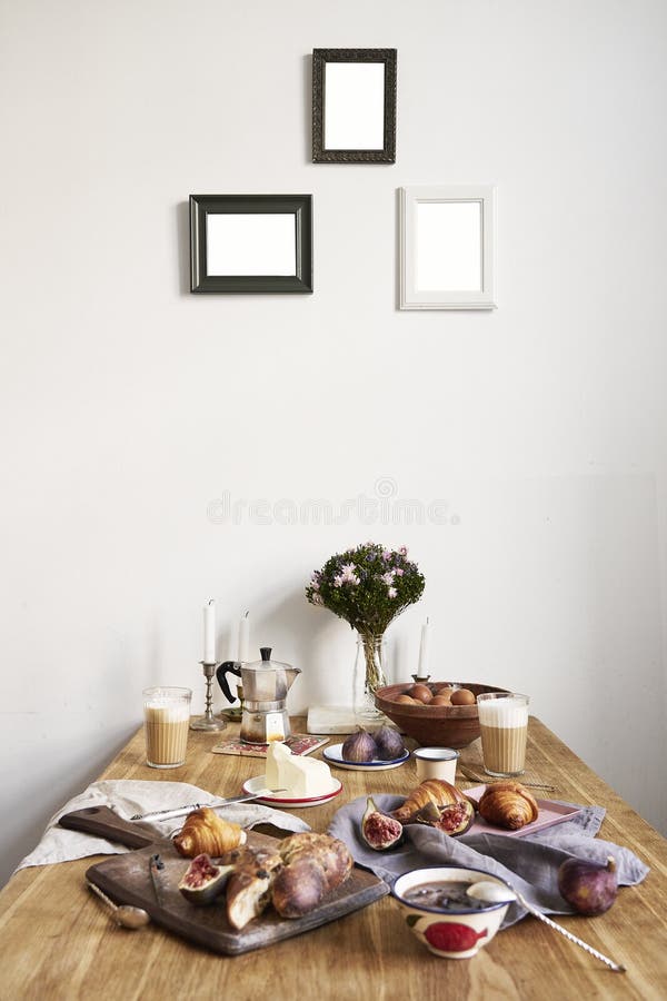 Breakfast in kitchen with photo frames on white wall. Croissants, figs, coffee, bread on wooden table background, empty space for layout. Breakfast in kitchen with photo frames on white wall. Croissants, figs, coffee, bread on wooden table background, empty space for layout