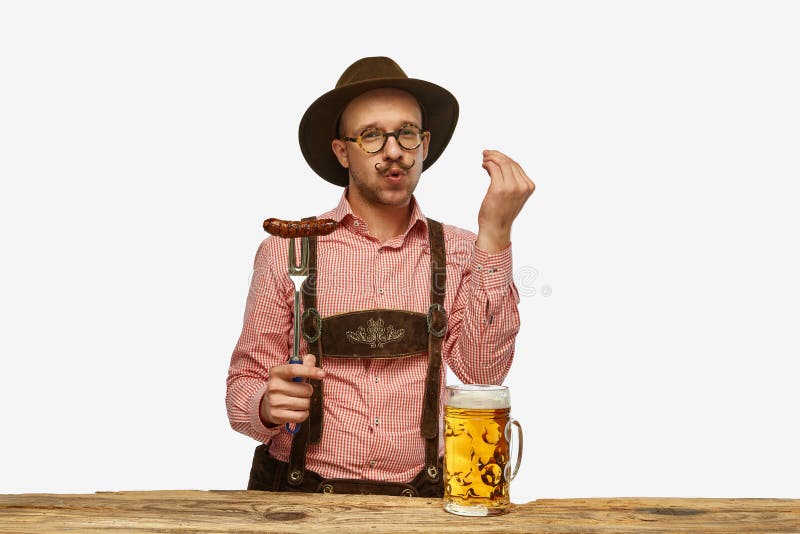 Young man wearing traditional fest Bavarian or German outfit with big beer glass and fried sausage celebrating Oktoberfest. Alcohol, traditions, holidays, taste concept. Copy space for ad. Young man wearing traditional fest Bavarian or German outfit with big beer glass and fried sausage celebrating Oktoberfest. Alcohol, traditions, holidays, taste concept. Copy space for ad