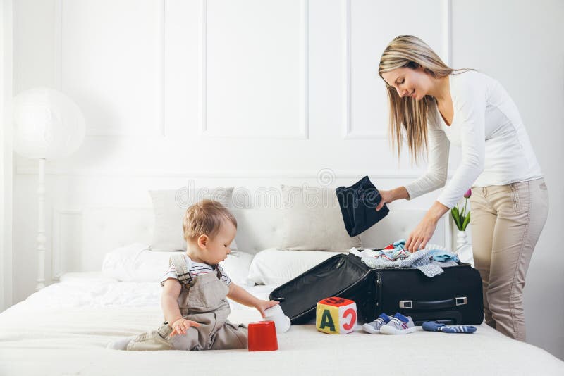Déplacement avec des enfants La mère heureuse avec son emballage d'enfant vêtx pour des vacances image libre de droits