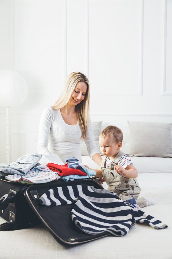 Déplacement avec des enfants La mère heureuse avec son emballage d'enfant vêtx pour des vacances image libre de droits