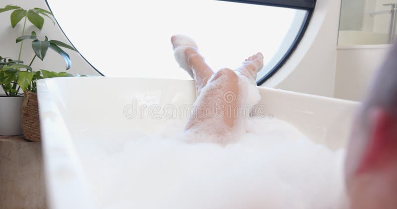Détendez-vous dans la baignoire d'une femme appréciant le bain à bulles avec jambes relevées banque de vidéos