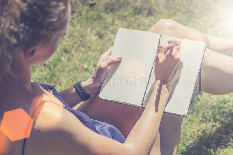 Día asoleado del verano Primer de un cuaderno en las manos de una mujer joven que se sienta en el parque en el césped foto de archivo libre de regalías