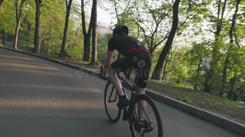 Dünner athletischer Radfahrer, der auf Rennrad im Park absteigt Radfahrer, der die schwarze Ausstattung fährt schwarzes Fahrrad t