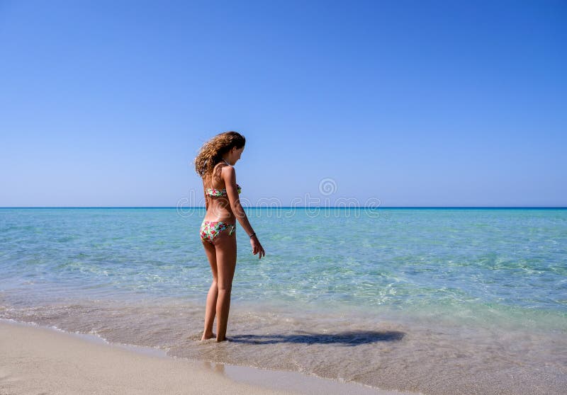 Dünnes und hübsches Mädchen in einer bunten Bikinistellung auf einem wunderbaren Strand mit haarscharfem Wasser lizenzfreies stockbild Dünnes und hübsches Mädchen in einer bunten Bikinistellung auf einem wunderbaren Strand mit haarscharfem Wasser lizenzfreies stockbild