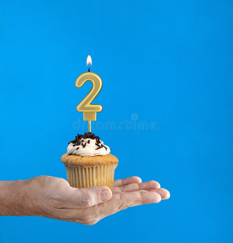 Hand holding a cupcake with the number 2 candle - Birthday on blue background. Hand holding a cupcake with the number 2 candle - Birthday on blue background