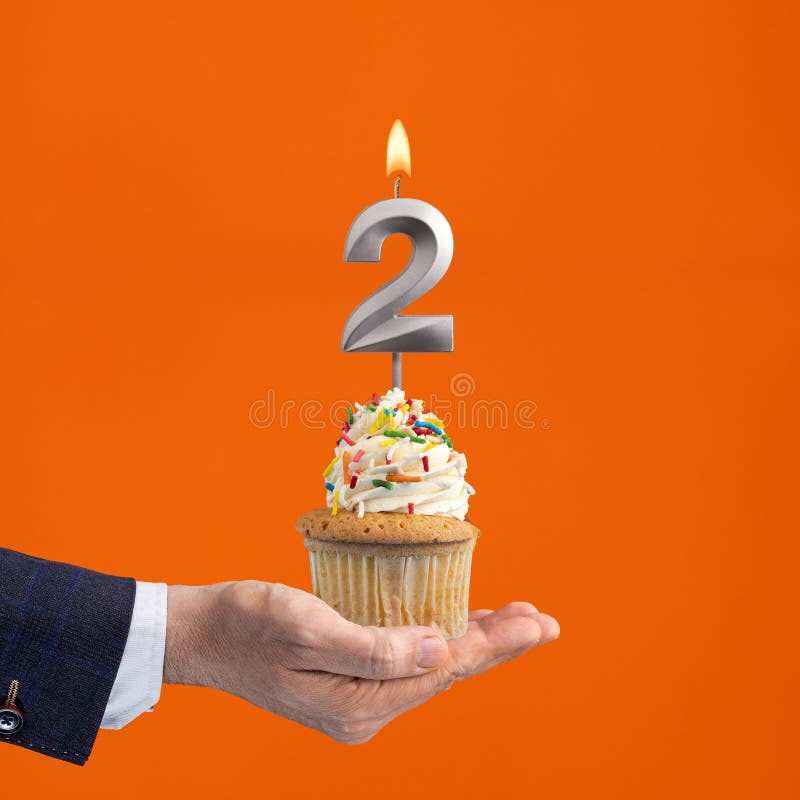 Hand holding birthday cupcake with number 2 candle - background orange. Hand holding birthday cupcake with number 2 candle - background orange