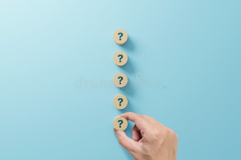 Hand holding wooden block shape with sign question mark symbol on blue background. Hand holding wooden block shape with sign question mark symbol on blue background