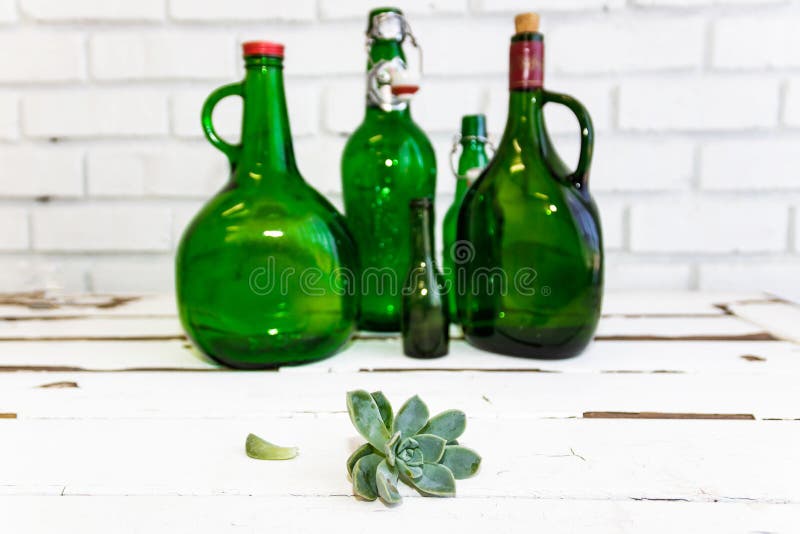 Vintage green glass bottle and desert rose. Desert rose and vintage green glass bottle on vintage white washed wooden table and against a white brick wall