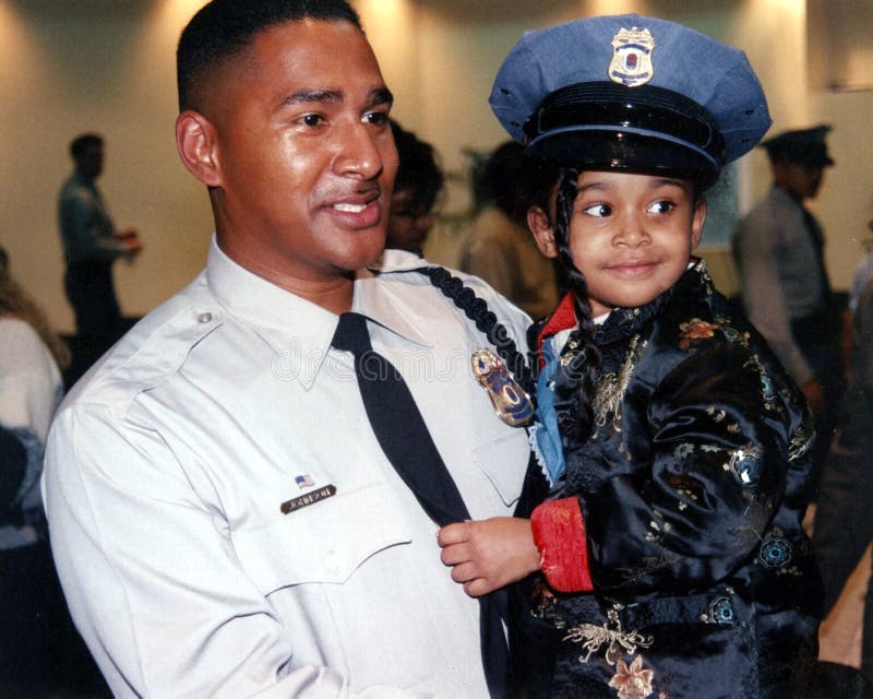 A brand new policeman who had just got sworn in at the Prince George`s s County Police graduation ceremony in Landover, Maryland is joined proudly by his little daughter who proudly wears his hat. A brand new policeman who had just got sworn in at the Prince George`s s County Police graduation ceremony in Landover, Maryland is joined proudly by his little daughter who proudly wears his hat