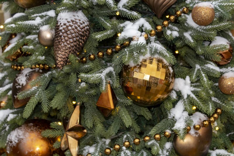 Christmas toys on the tree powdered with snow. New Year`s gold and brown toys on the tree powdered with snow