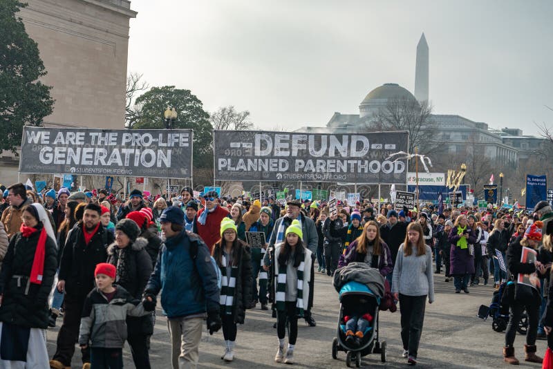 WASHINGTON D.C./USA - JANUARY 18, 2019: Pro-life supporters walk holding signs protesting abortion during the annual March for Life. WASHINGTON D.C./USA - JANUARY 18, 2019: Pro-life supporters walk holding signs protesting abortion during the annual March for Life