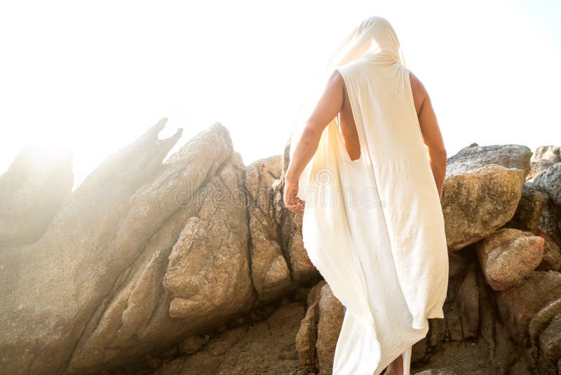 Fashion handsome guy at sunset posing in a white robe near the rocks.