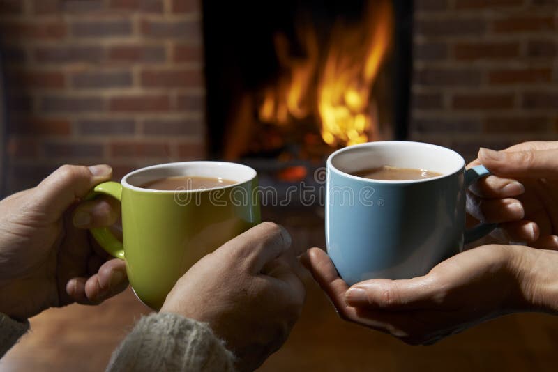 Couple Holding Hot Drinks Relaxing By Fire. Couple Holding Hot Drinks Relaxing By Fire