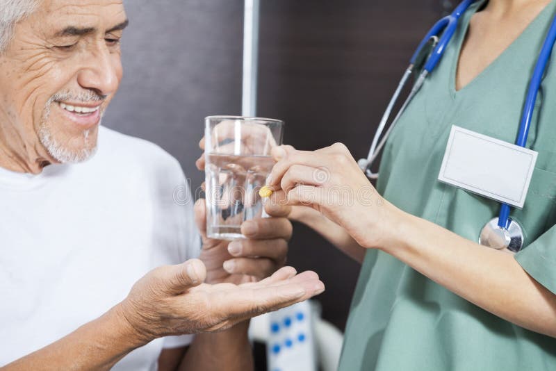 Midsection of nurse giving medicine and water to smiling male patient in rehab center. Midsection of nurse giving medicine and water to smiling male patient in rehab center