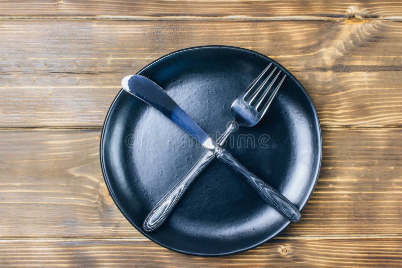 Intermittent fasting concept with knife and fork showing cross symbol on black plate, top view. Intermittent fasting concept with knife and fork showing cross symbol on black plate, top view
