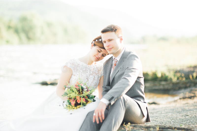 Brud och brudgum håller en vacker brudbukett. Poserar vid floden arkivfoto