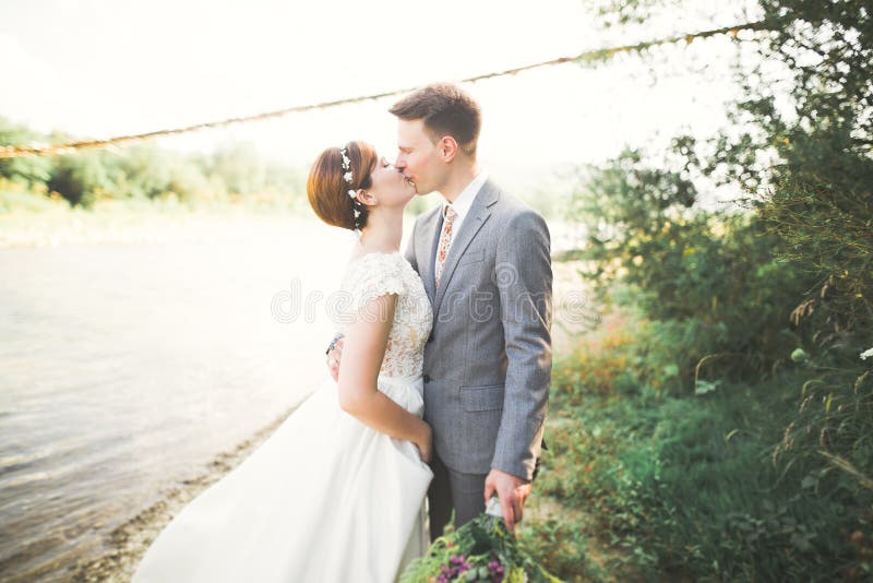 Brud och brudgum håller en vacker brudbukett. Poserar vid floden arkivfoton