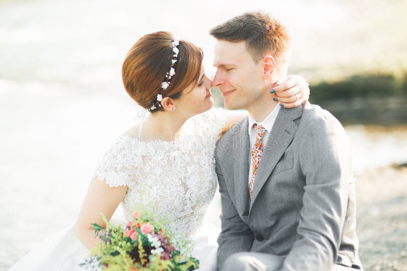 Brud och brudgum håller en vacker brudbukett. Poserar vid floden royaltyfri bild