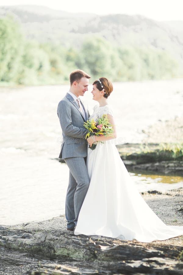 Brud och brudgum håller en vacker brudbukett. Poserar vid floden royaltyfria bilder