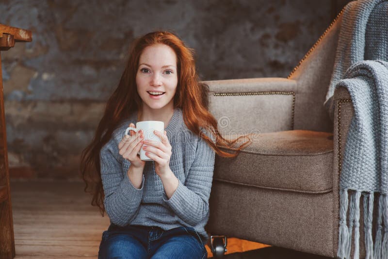 Happy young readhead woman drinking hot coffee or tea at home. Calm and cozy weekend in winter or autumn. Happy young readhead woman drinking hot coffee or tea at home. Calm and cozy weekend in winter or autumn