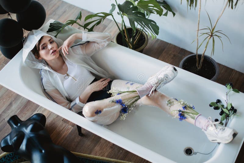 Ritratto di moda di una ragazza in abiti di plastica Stile ecologico Modello giacente nel bagno fotografie stock