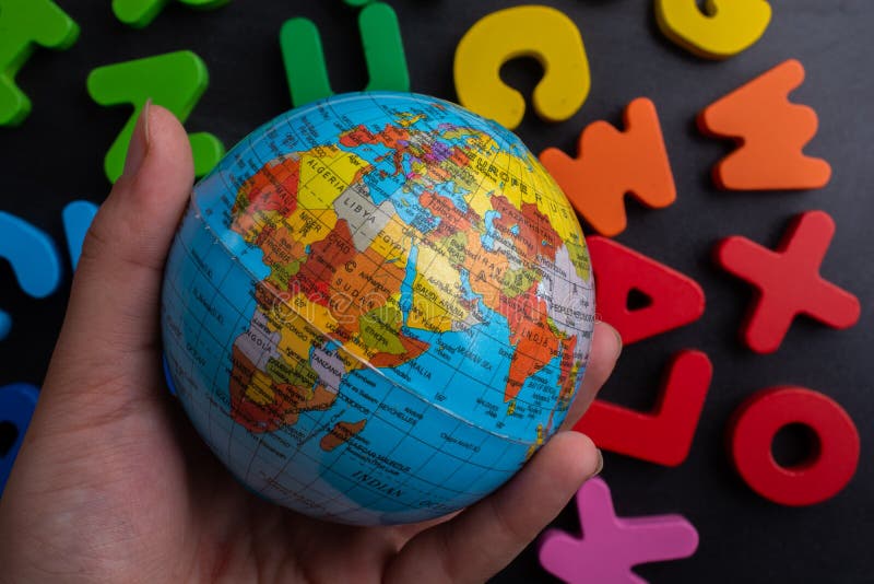 Mão segurando um modelo de globo terrestre sobre letras coloridas em fundo preto fotografia de stock