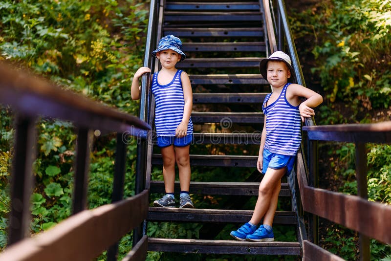 Two Boys in Striped T-shirts and Blue Shorts Stand on the Stairs in the ...