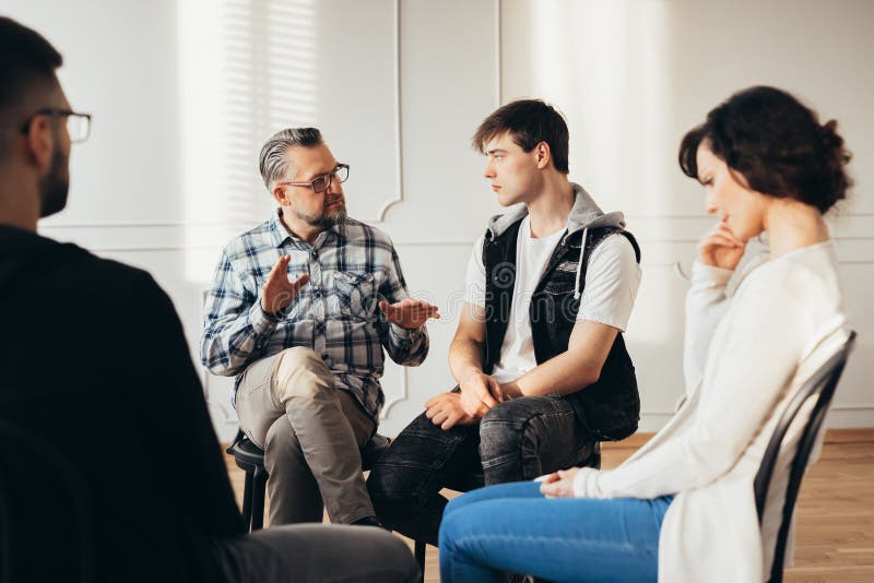 Psychologist talking about twelve-step program to addicted men during group meeting. Psychologist talking about twelve-step program to addicted men during group meeting