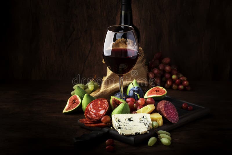 Red wine glass and appetizers, cheese, salami, figs, grapes, vintage wooden table  background, selective focus, copy space. Red wine glass and appetizers, cheese, salami, figs, grapes, vintage wooden table  background, selective focus, copy space