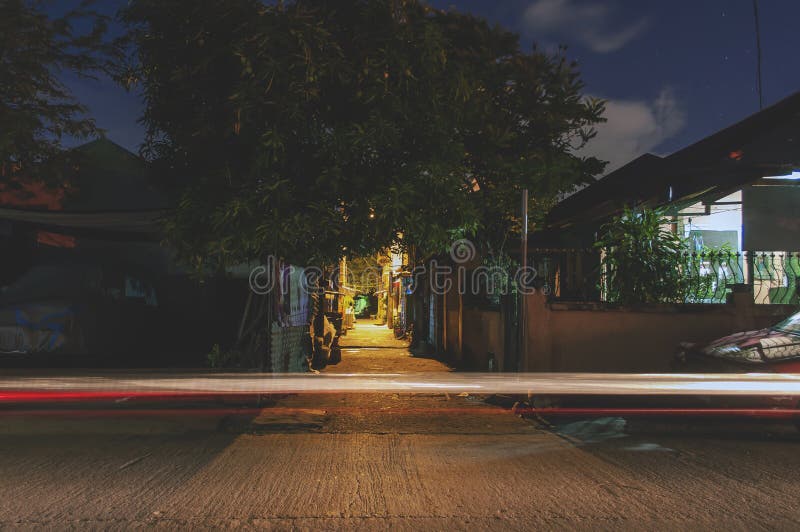 Long exposure night shot of an alley right in the middle of the scene entering the street with single light trail from a car`s headlight. Long exposure night shot of an alley right in the middle of the scene entering the street with single light trail from a car`s headlight.