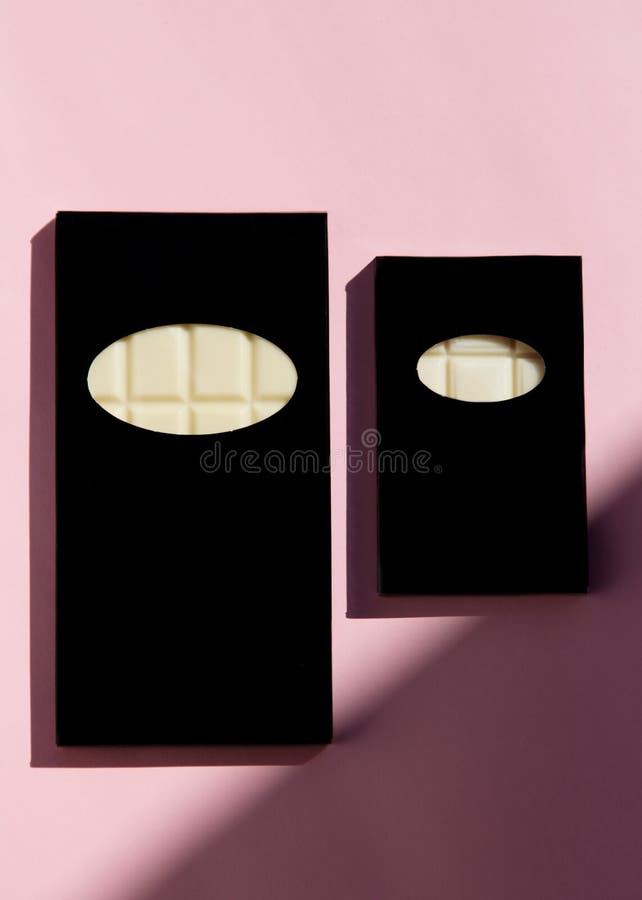 Bars of white chocolates on a pink background. Two bars of white chocolates in black packaging lies on a pink background