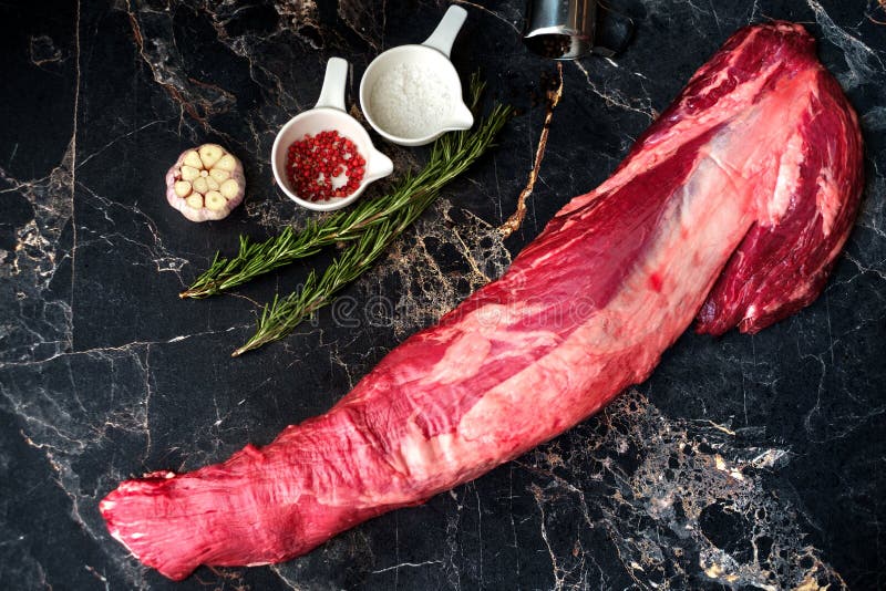 Fresh raw beef tenderloin on a marble table with seasonings and rosemary, a whole uncut piece. Fresh raw beef tenderloin on a marble table with seasonings and rosemary, a whole uncut piece