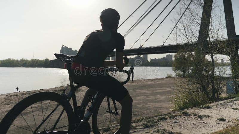 Sportsportler mit starker Passform, der auf dem Fahrrad sitzt und weit voraus schaut Cyclist träumt von Zukunft Brücke und Fluss