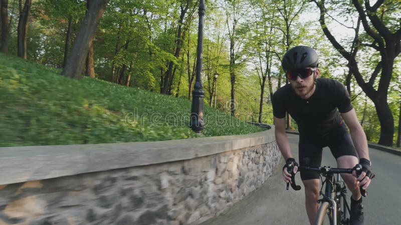 Stark sportlicher Radfahrer, der bergauf aus dem Sattel springt Fahrradfahrer auf steigendem Hügel mit schwarzer Sportbekleidung