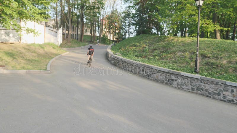 Stark sportlicher Radfahrer, der bergauf aus dem Sattel springt Fahrradfahrer auf steigendem Hügel mit schwarzer Sportbekleidung