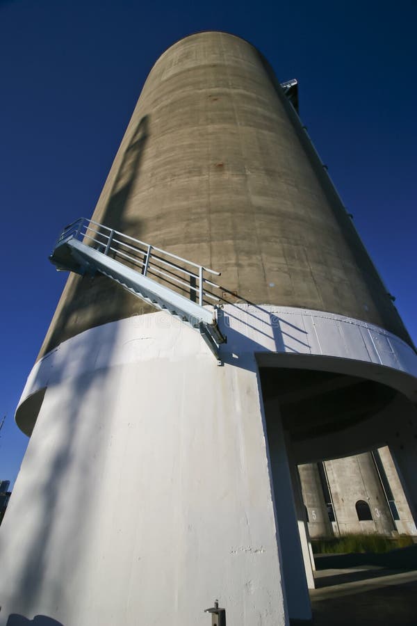 Urban landscape of rising gray concrete silo into sky like a rocket. Decommissioned grey cylindrical gas and oil repository tower. Towering storage tank architecture on brownfield. Industrial depository at popular tourist attraction. Tower structure in city garden. Old circular storehouse building renovated into architectural landmark. Urban landscape of rising gray concrete silo into sky like a rocket. Decommissioned grey cylindrical gas and oil repository tower. Towering storage tank architecture on brownfield. Industrial depository at popular tourist attraction. Tower structure in city garden. Old circular storehouse building renovated into architectural landmark.